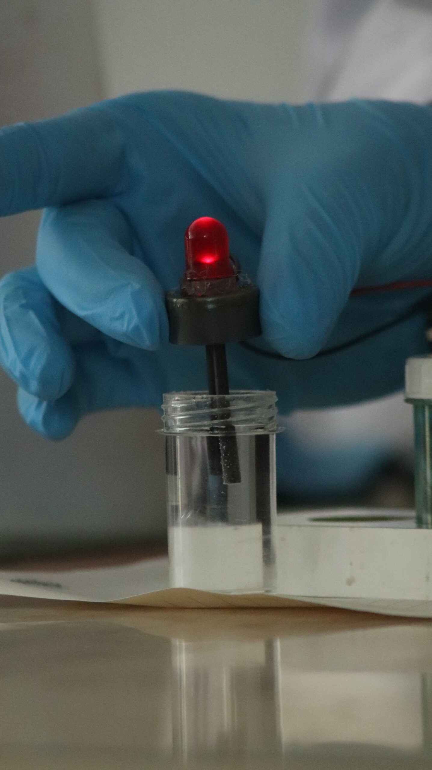 A gloved hand operates a red LED indicator in a laboratory setting, showcasing precise scientific experimentation.